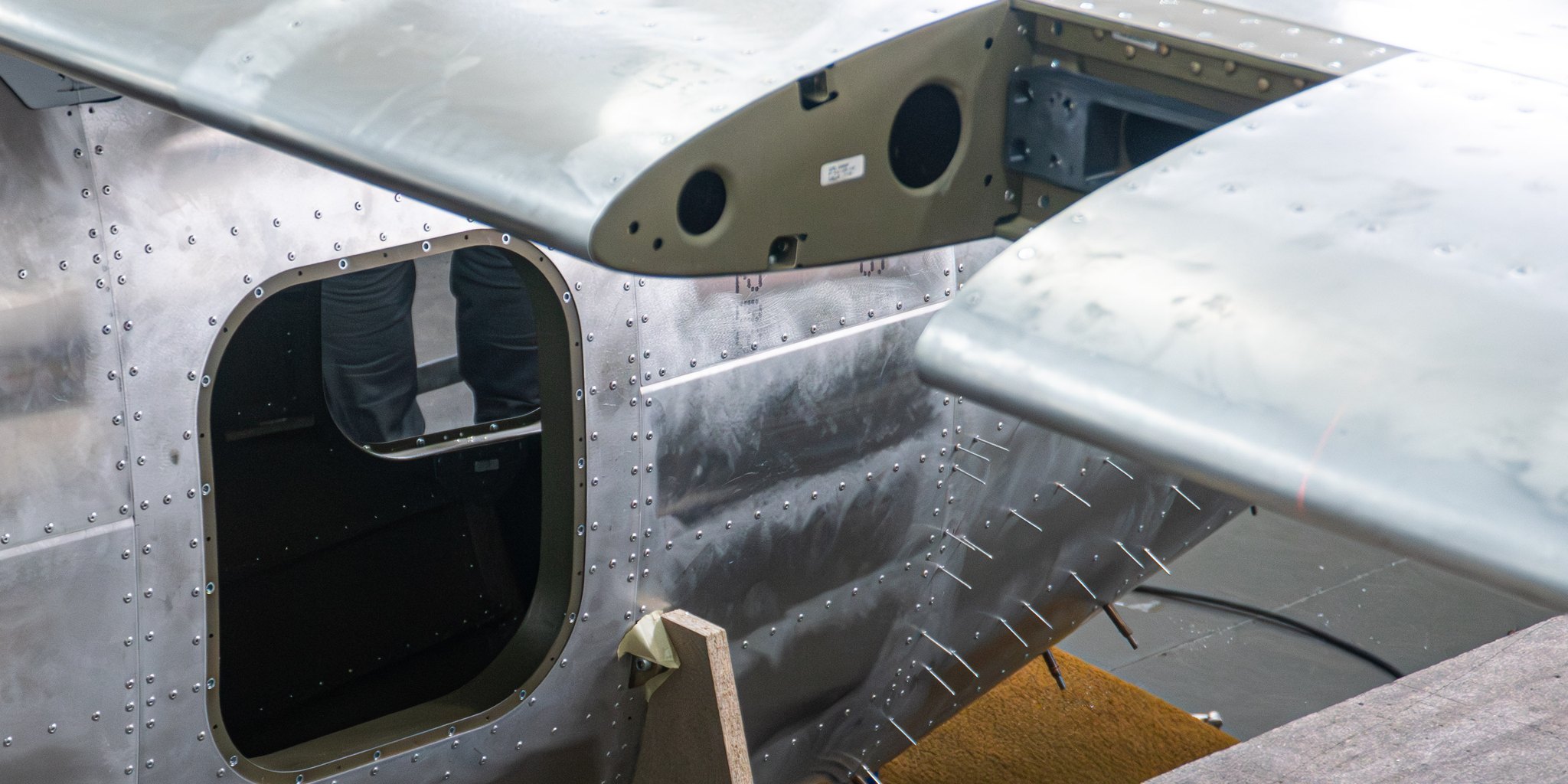 The TD 2.0 fuselage skin and wing root in bare aluminum, rivet lines and temporary cleco fasteners still in place
