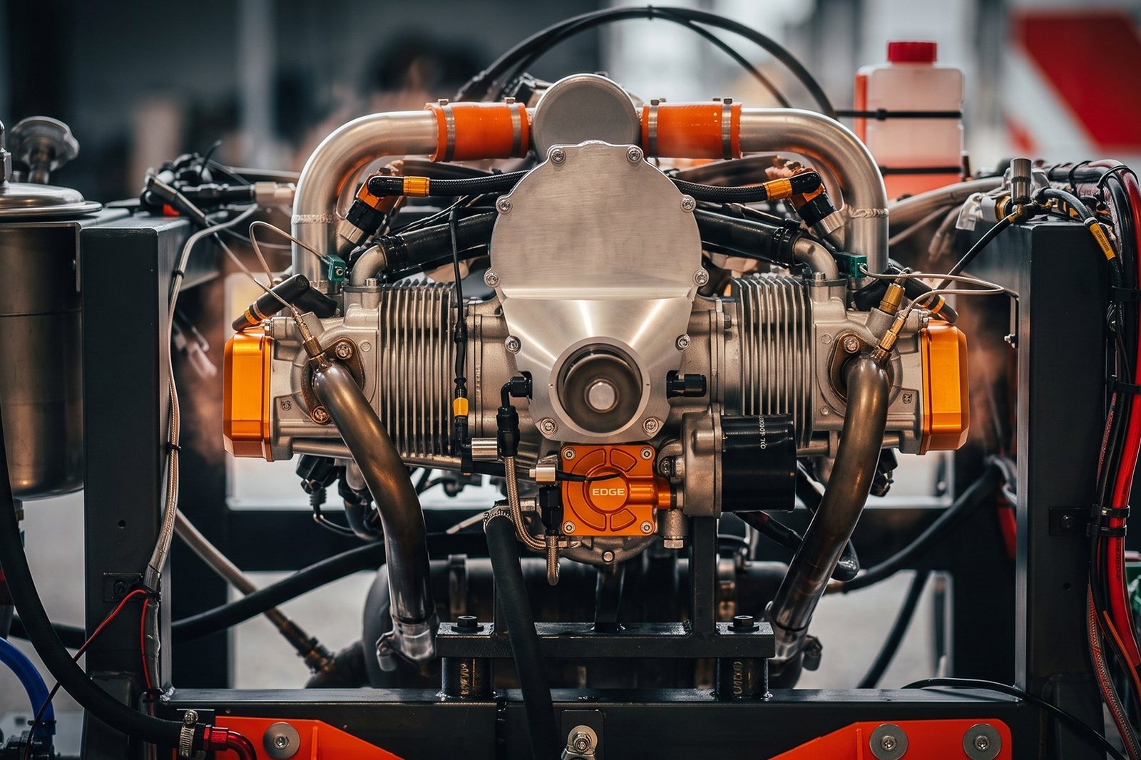 The Technology Demonstrator 2.0 piston engine running on a test stand, polished exhaust headers, orange couplers and instrumentation wiring around it