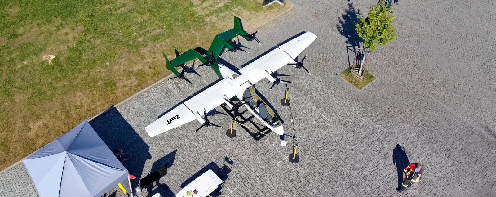 The Zuri display aircraft seen from above on the expo apron, rotors and green tail booms spread across the paving