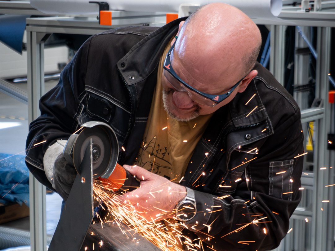 A Zuri technician grinding a steel bracket in the workshop near Prague, sparks flying, safety glasses on