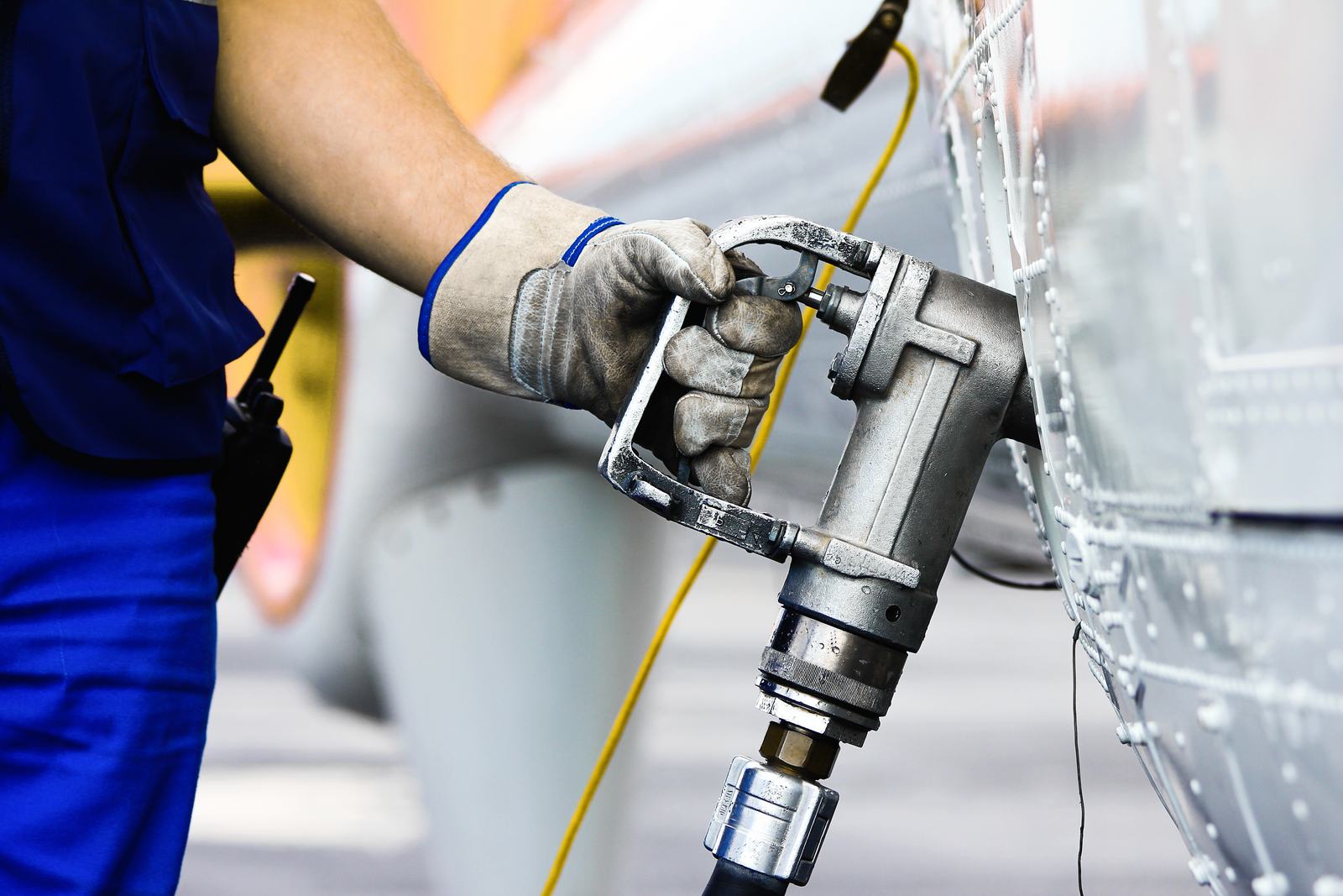 A gloved hand holding a fuel nozzle in an aircraft's refueling port on the apron