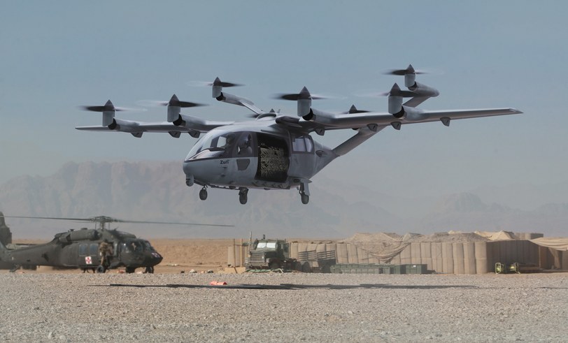 Render of the aircraft in gray military livery holding a hover over a desert forward base, helicopters and vehicles behind it