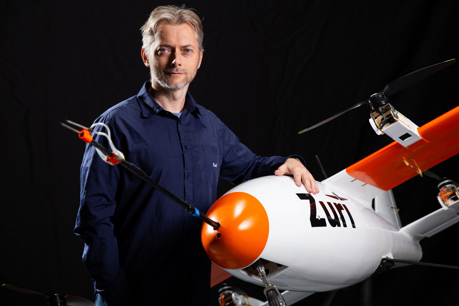 Zuri founder and CEO Michal Illich beside a subscale demonstrator, one hand on its nose, against a black studio backdrop