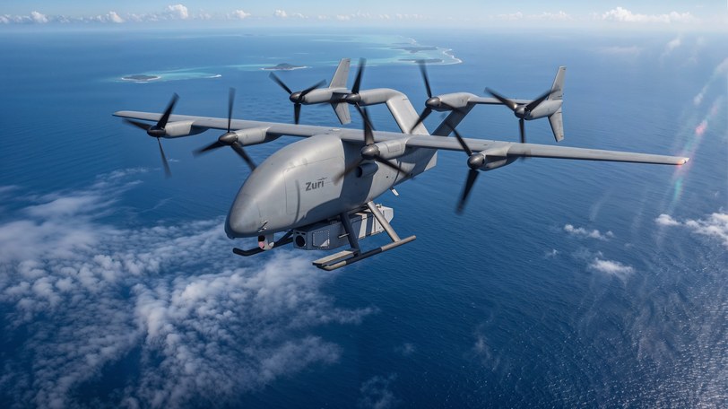 Render of the uncrewed cargo aircraft above a cloud layer, coral atolls and shallow reef water visible beneath