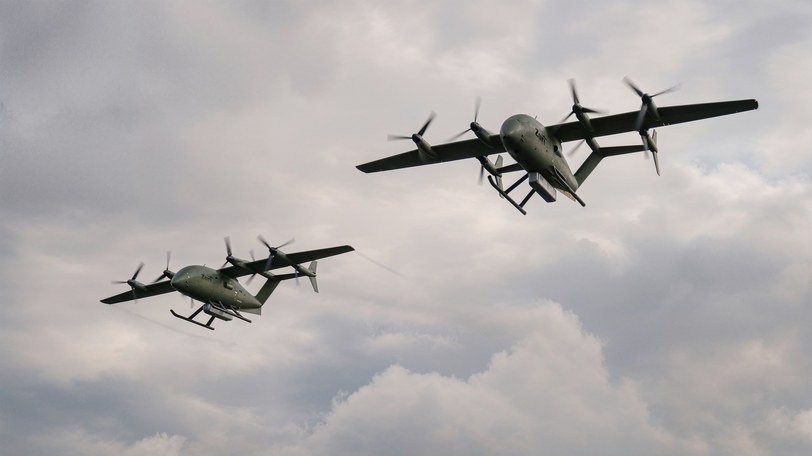Render of two Zuri aircraft in olive defense livery flying through broken cloud, one above and behind the other