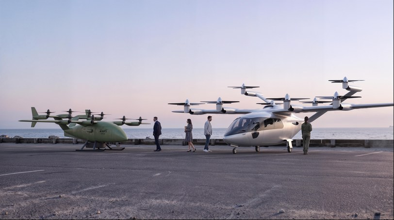 Render of the olive uncrewed cargo aircraft and the white six-seat passenger aircraft parked apart on a coastal quay at sunset, four people walking between them
