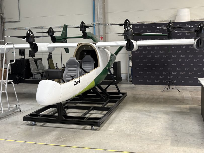 The Zuri display aircraft on its wheeled stand, cockpit open with two seats visible and propulsion booms fitted