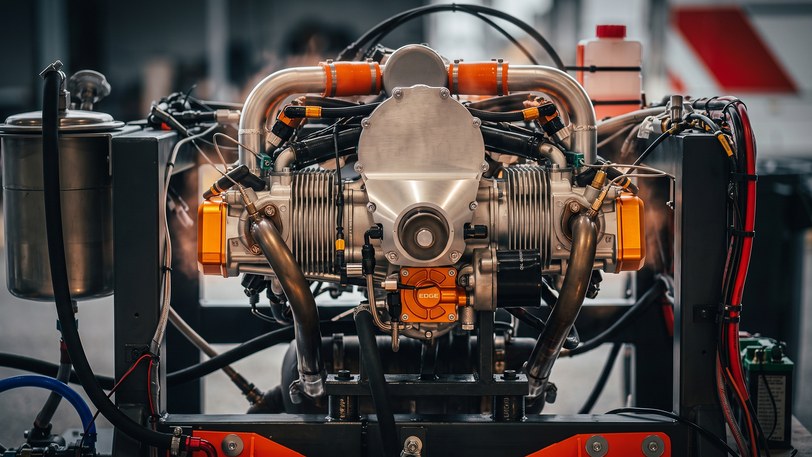 The Technology Demonstrator 2.0 piston engine running on a test stand, polished exhaust headers, orange couplers and instrumentation wiring around it