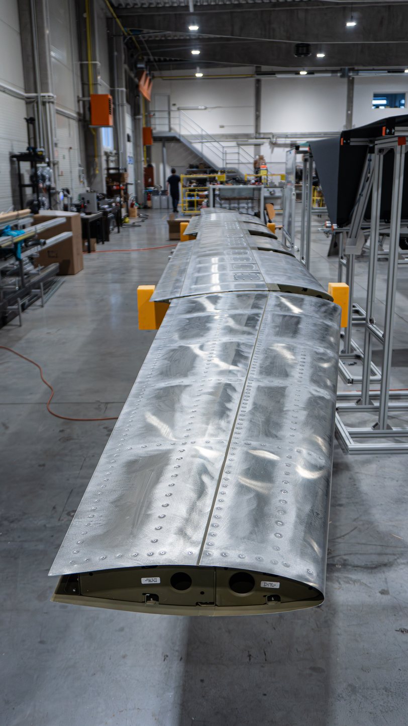A bare aluminum TD 2.0 wing resting on trestles in the Prague hall