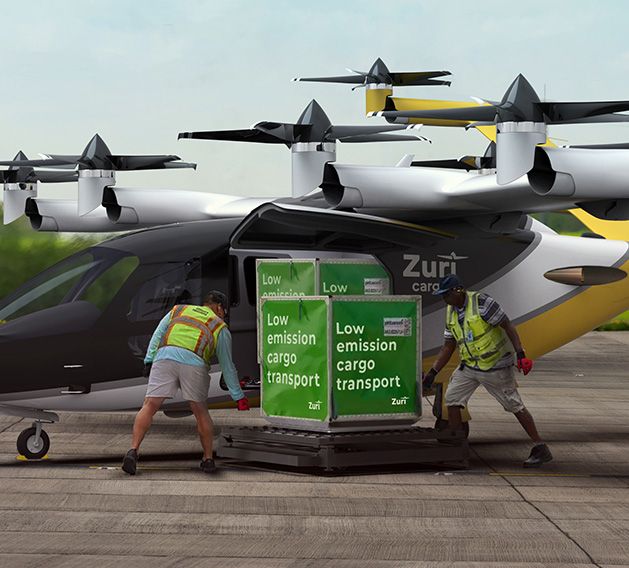 Two ground crew members loading a green-labeled cargo container marked 'Low emission cargo transport' into a Zuri Hybrid VTOL aircraft at an airport.