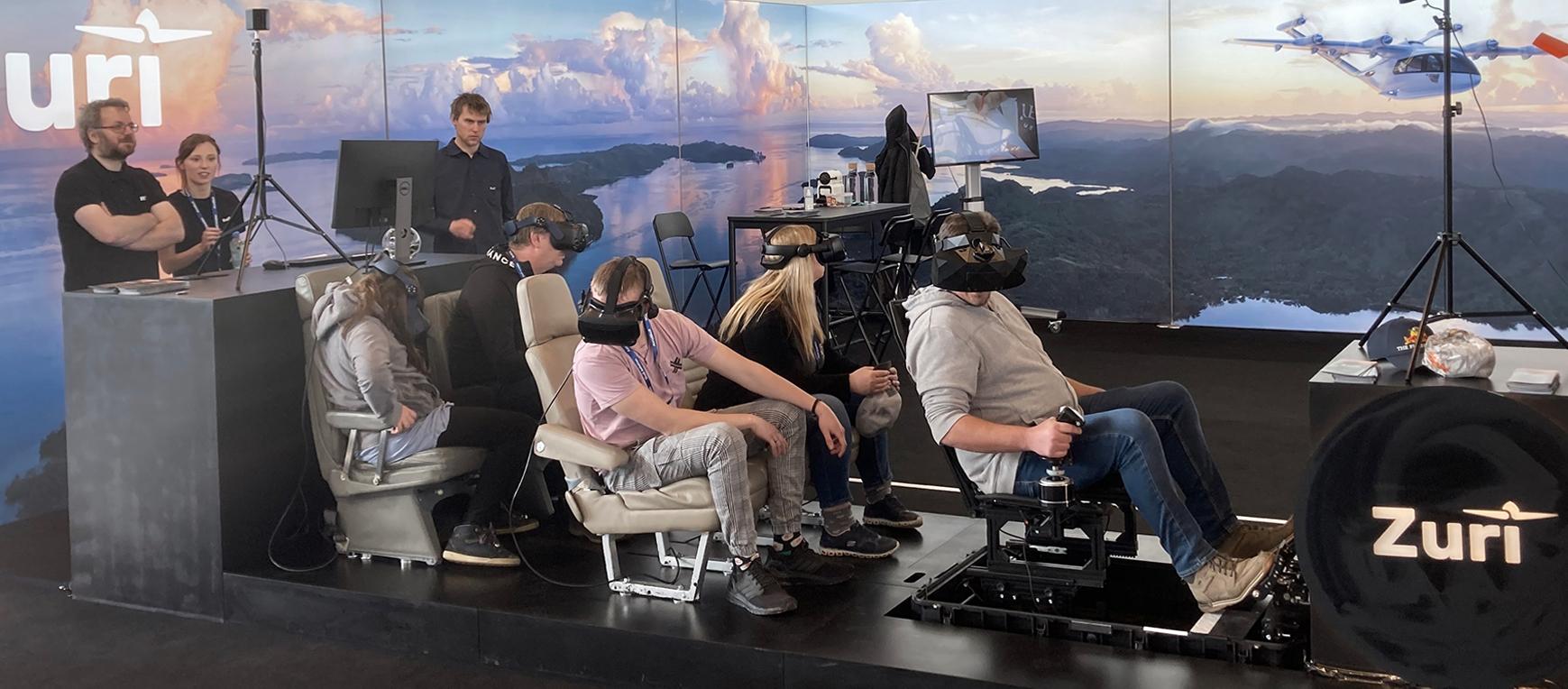 Visitors experience Zuri’s 5-person VR flight simulator at the AERO Conference, showcasing the capabilities of hybrid VTOL aircraft with one pilot in control and four passengers onboard.