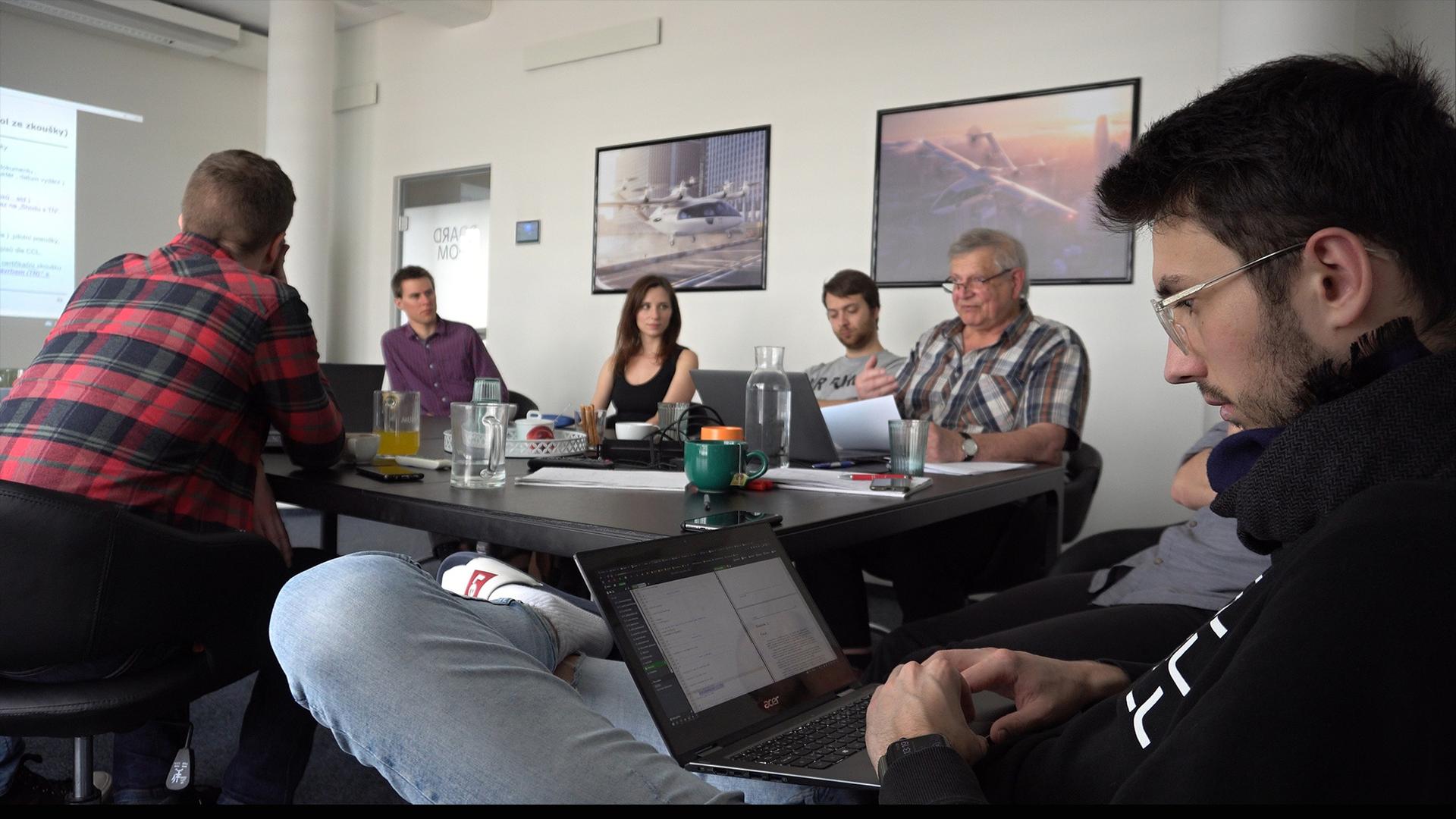 Zuri team members engaged in a strategy meeting around a conference table with aircraft posters on the wall.