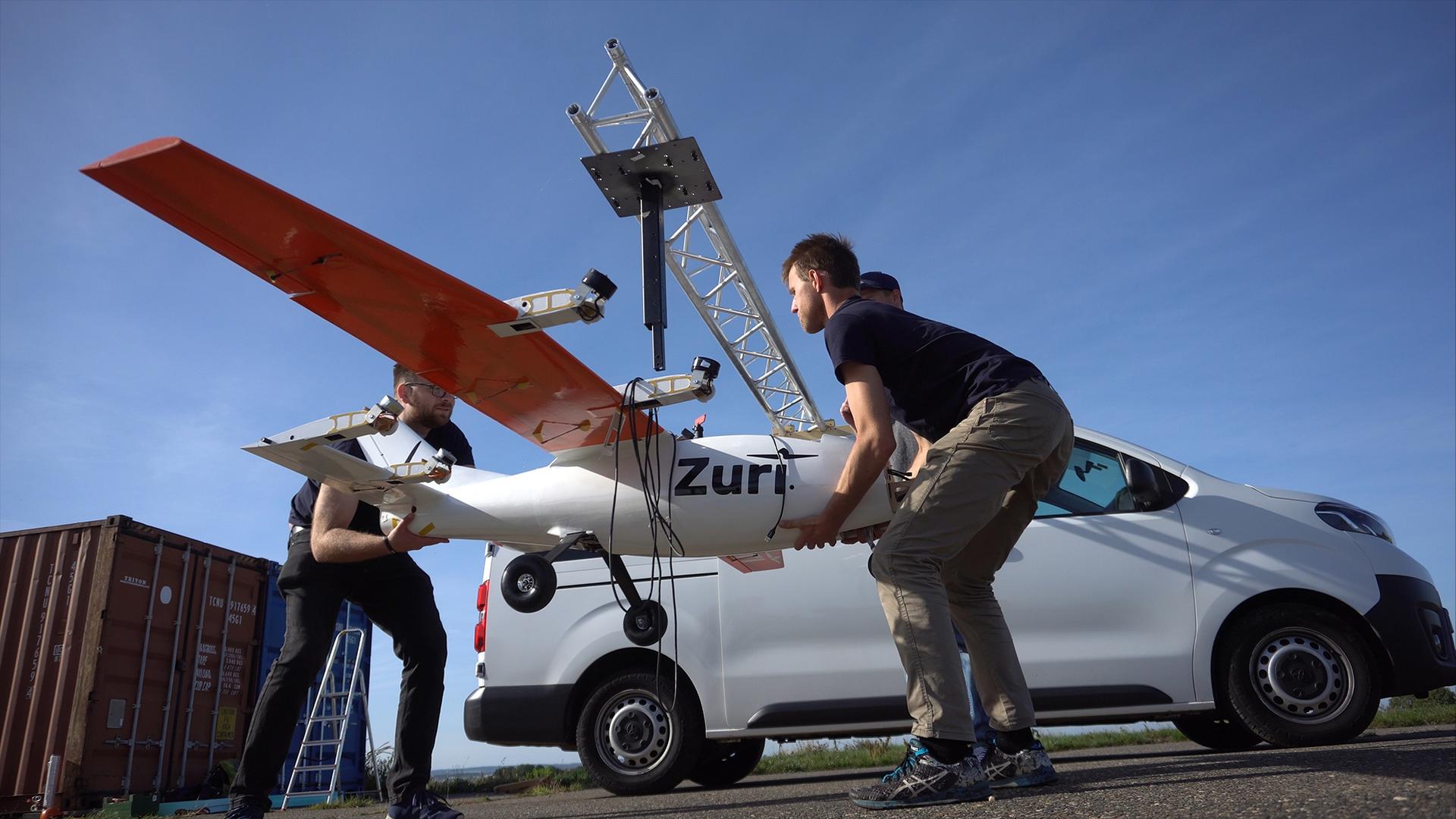 Zuri engineers handling a test aircraft during outdoor field setup under a clear blue sky.
